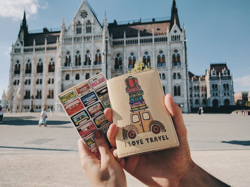Hands holding travel-themed passports with Budapest Parliament in the background.
